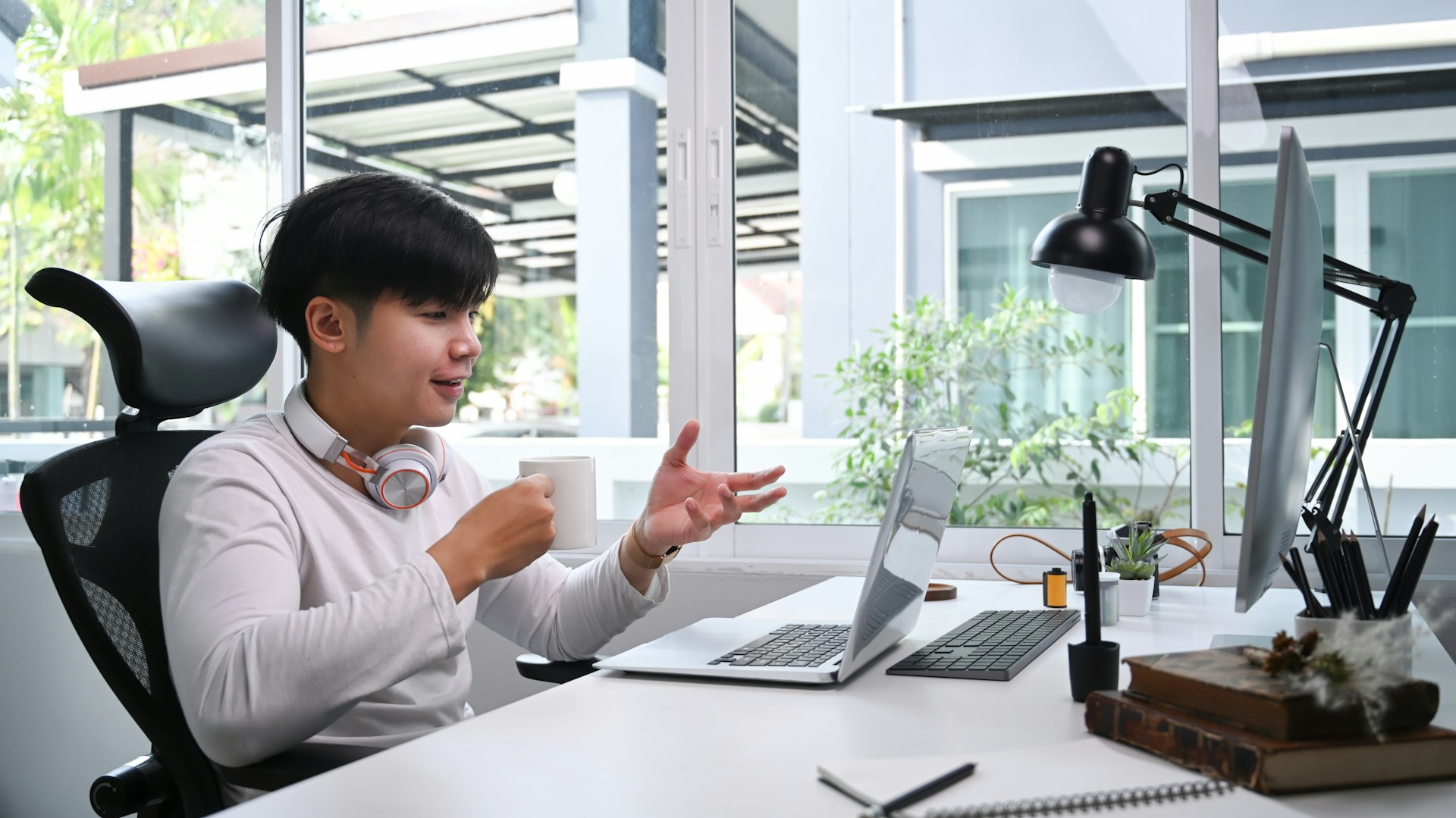 A young man talking and gesturing while looking at a laptop in an office.